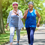 Two people smiling while walking briskly on a path.