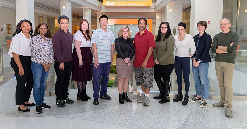 Eleven people stand in a line smiling for the camera. They are in the atrium of a building.