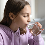 Teen girl drinking clear liquid from a clear glass.