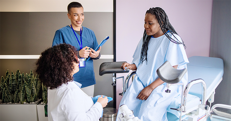 A woman sitting on an examination table interacts with two health care providers.