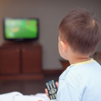 A young child with a remote control in his hand looking at a television screen.