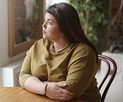 A young woman with overweight sitting at a table and looking through a window.