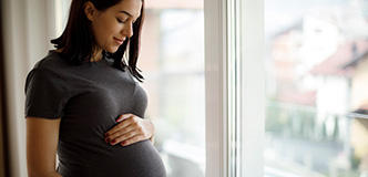 Una persona embarazada con las manos en el abdomen, parada delante de una ventana.