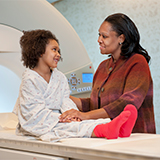 Parent reassuring child on table in front of scanner.