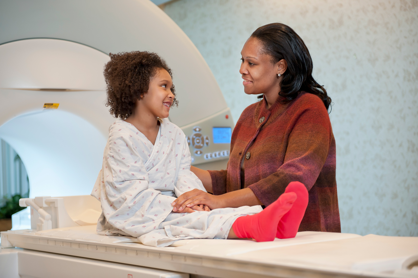 Parent reassuring child on table in front of scanner.