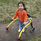 Toddler standing, holding the rails of an assisted walking device.