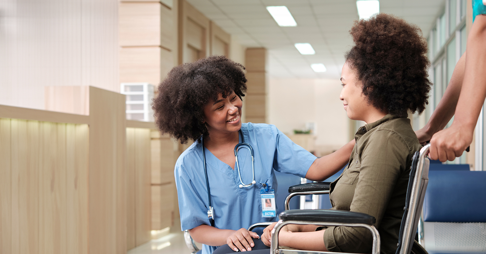 Medical professional with stethoscope attends to pregnant person in wheelchair.