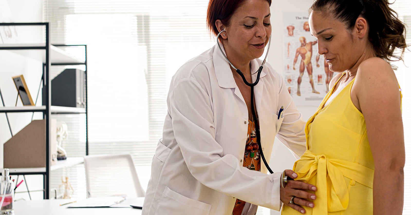 Health care professional with a stethoscope examining a pregnant woman.