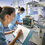 Technicians taking notes from screen monitor of a preterm infant in an isolette.