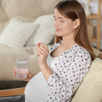 A pregnant woman holding a glass of water and a tablet, presumably vitamin D.
