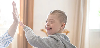 A boy with Down syndrome gives his mother a high five. Text overlay: “Drive Down Syndrome Research With Your Unique Story”.