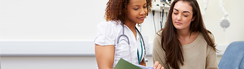 A nurse and a female patient reading a medical booklet together in an examining room.