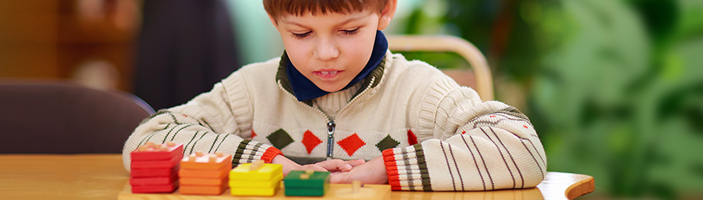 A boy looking down at colored wooden blocks.	