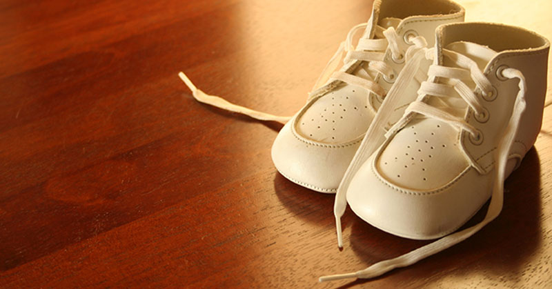 A pair of white baby shoes setting on a hardwood floor.