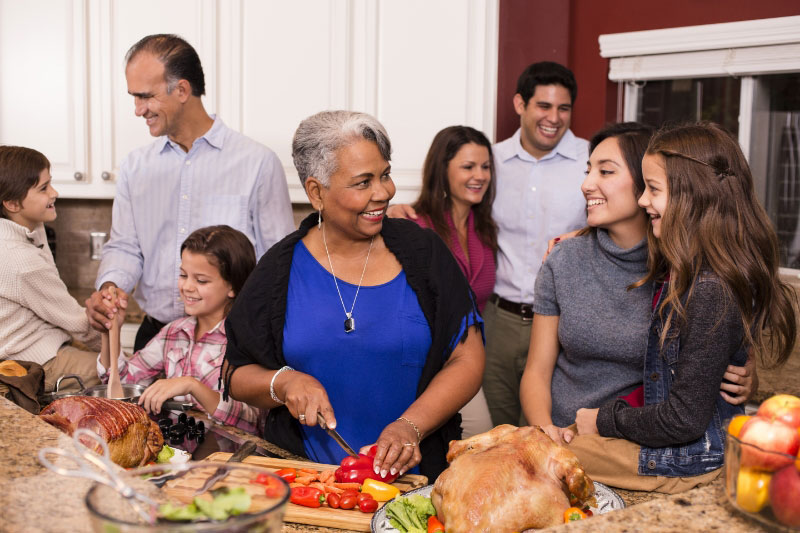 Multi-ethnic, multi-generational family members prepare a holiday dinner together in their home kitchen.