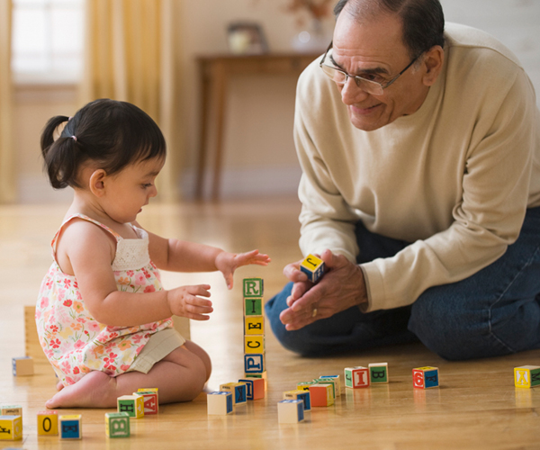 Image of a grandfather smiling at a toddler playing with alphabet blocks. 