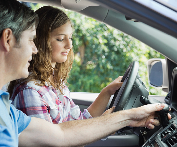 Image of a father showing his teenage daughter the gears to operate a car. 