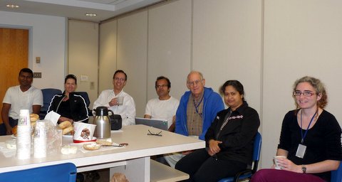 Seven lab members sit around a large table with refreshments on it. 