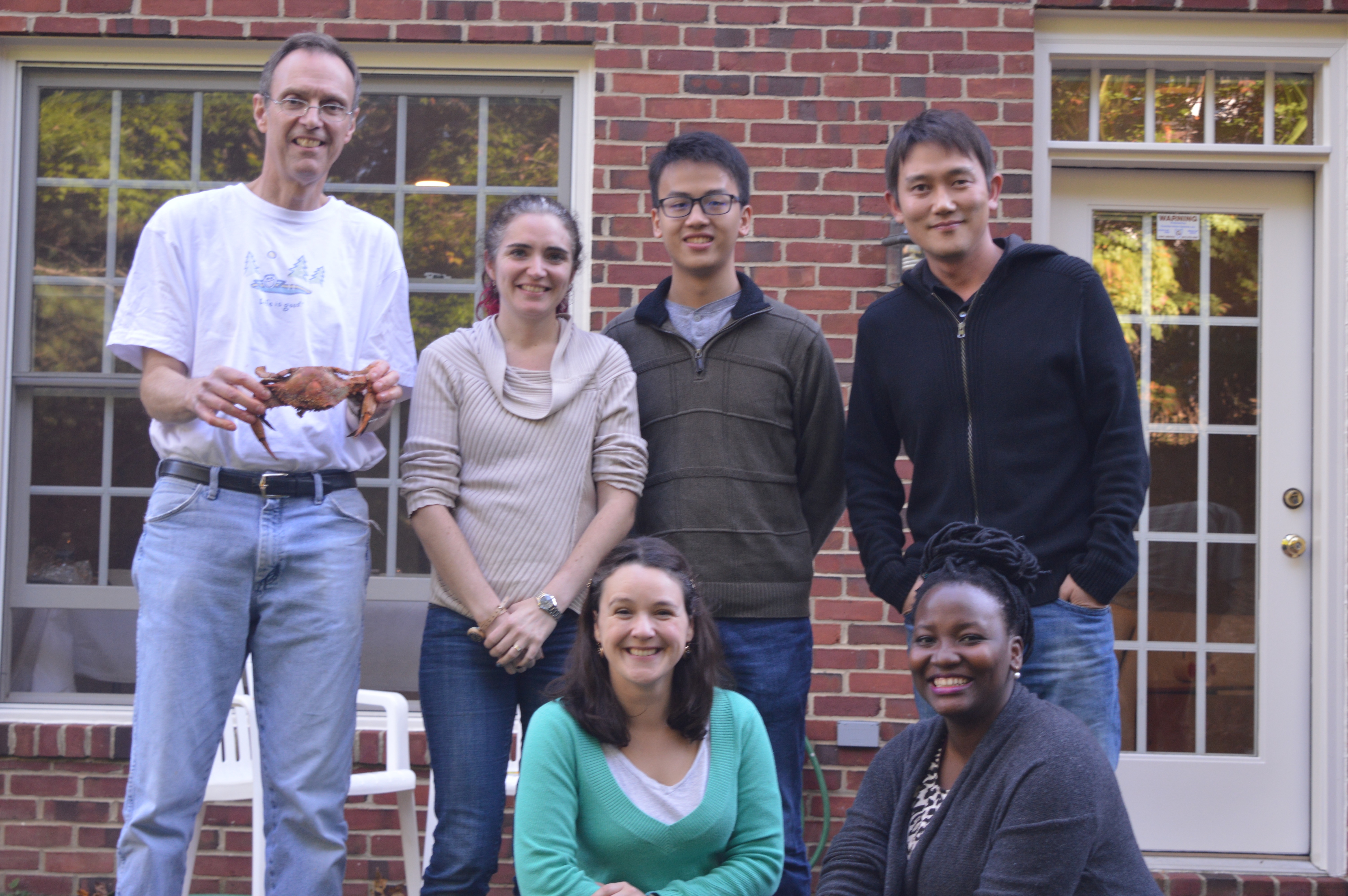 Members of the Levin lab outside of a brick building. Dr. Levin is holding a crab up.