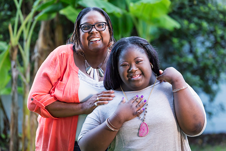 A young woman with Down syndrome smiles with her grandmother in an outdoor setting.