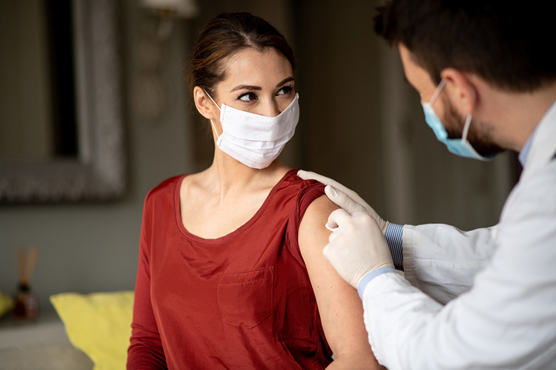 Health care worker swabbing a patient’s arm for a vaccination. Both are wearing masks.