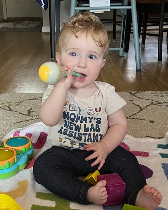 A cute toddler sits on a carpet while chewing a toy. 