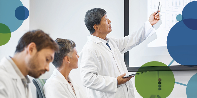 A scientist pointing at a screen leads a presentation before other scientists.