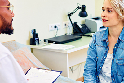 Healthcare provider speaking to a female patient in an exam room.