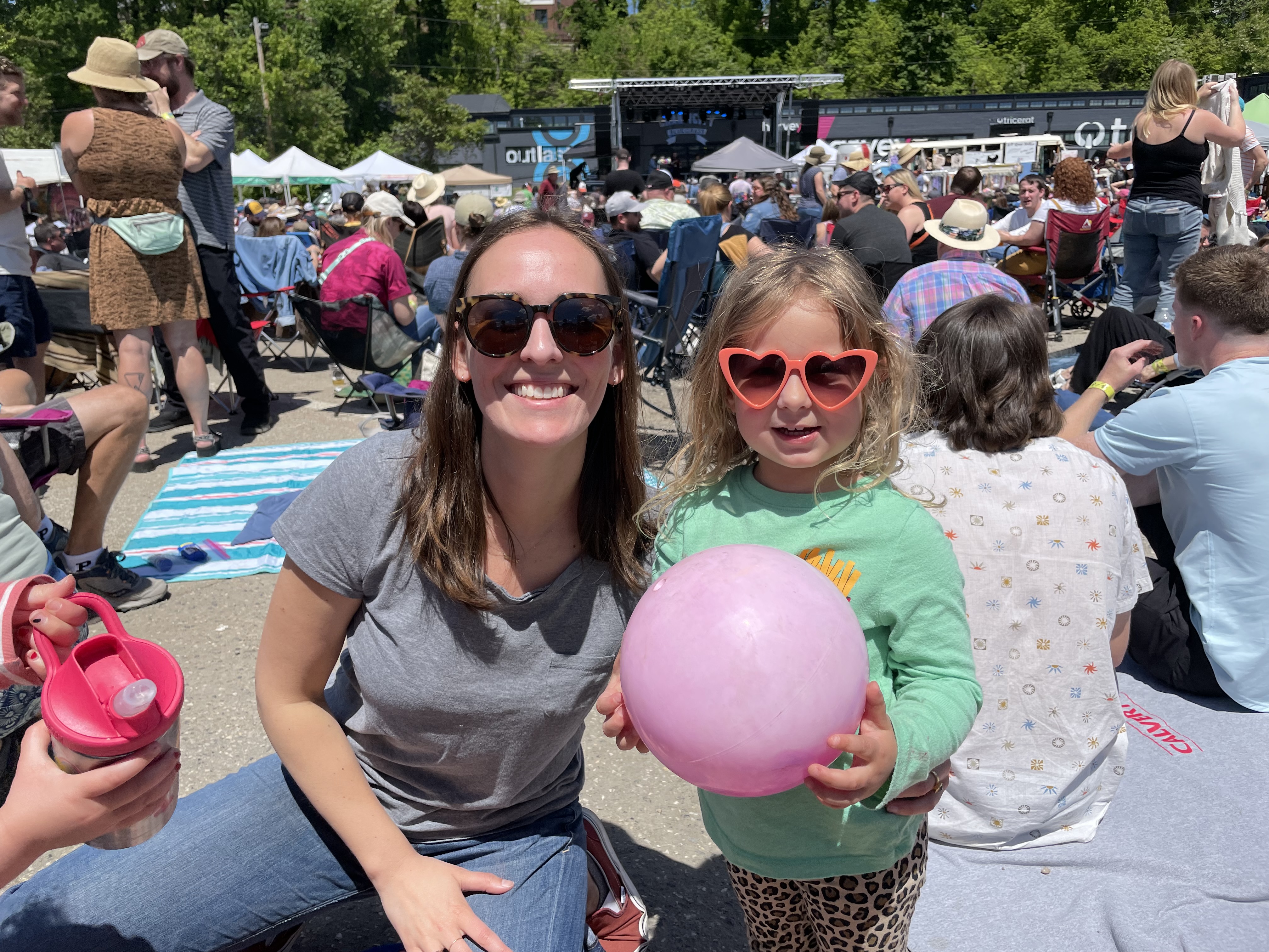 A woman and a young child holding a balloon smile at the camera. A crowd of people and stage are visible in the background.