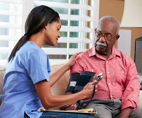 A nurse takes the blood pressure of an elderly man. Both are African-American.