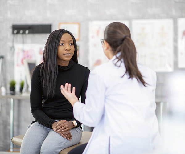 A woman sits in an exam room listening to a healthcare provider.