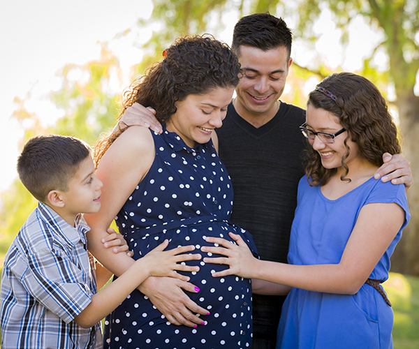 Family gathered around pregnant woman. The pregnant woman’s daughter and son are holding their hands against her stomach.