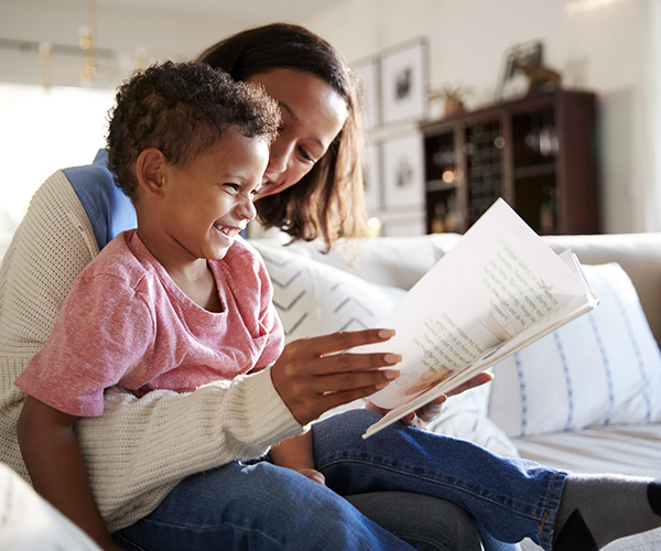 A little boy sits in a woman’s lap, laughing as she reads to him.