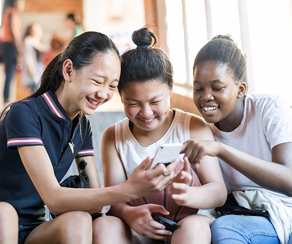 Three teenaged girls laugh as they all look at one of their mobile devices.