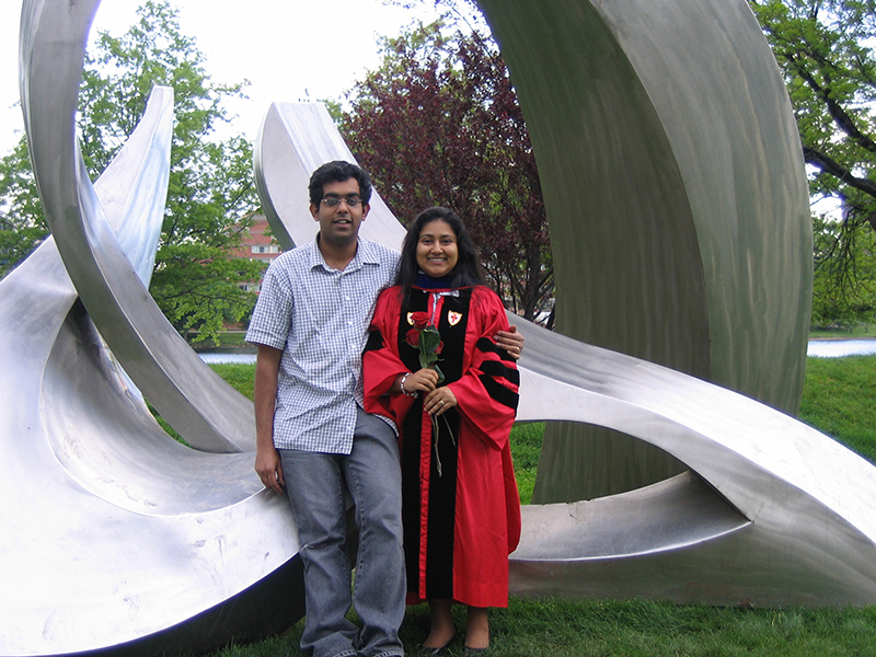 A smiling couple stands in front of an abstract sculpture.