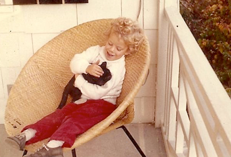 She sits outside holding and petting her cat with a smile on her face.