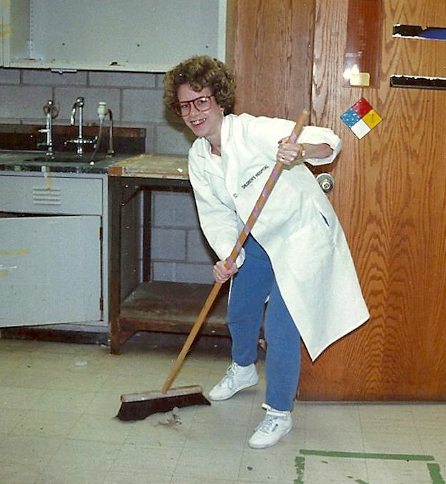 Dr. Bianchi smiles for the camera as she sweeps the floor with a large broom. 
