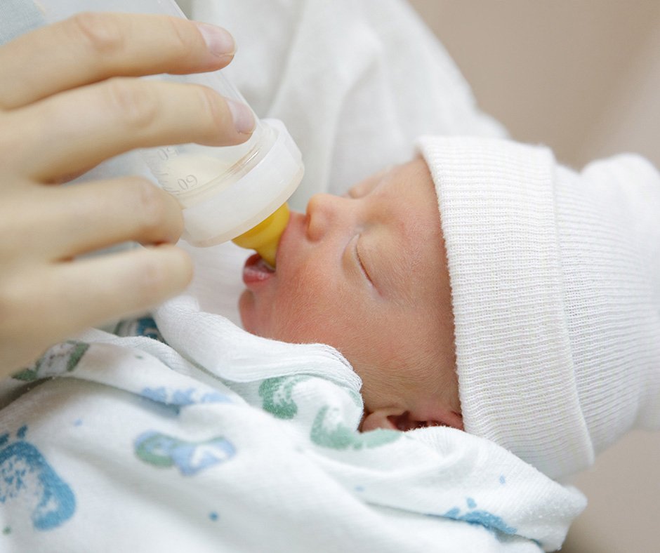 An adult feeding an infant child milk from a bottle.