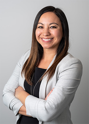 A smiling woman stands against a neutral background.