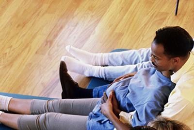 A pregnant woman and her partner sit together on a floor mat in a labor and delivery class.