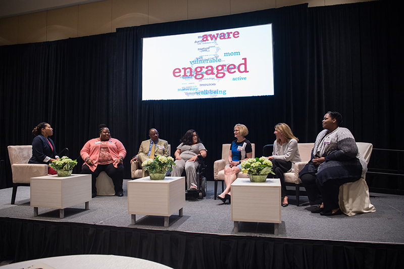 Community members and staff sit together on stage at the Improving Maternal Health Community Engagement Forum.