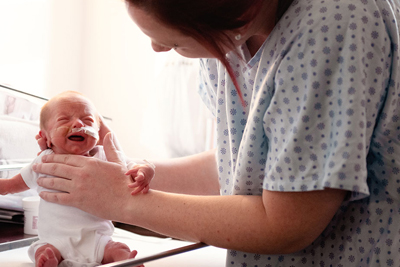 A mother holds her baby in an upright position. 