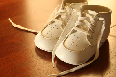 A pair of white baby shoes setting on a hardwood floor. 