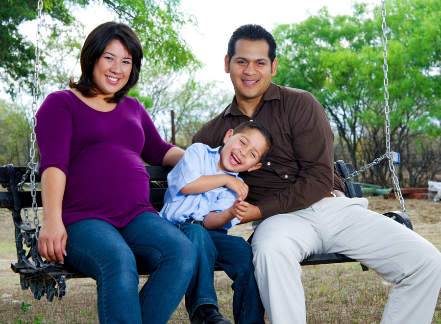 A pregnant woman and a man, with a laughing boy seated between them.