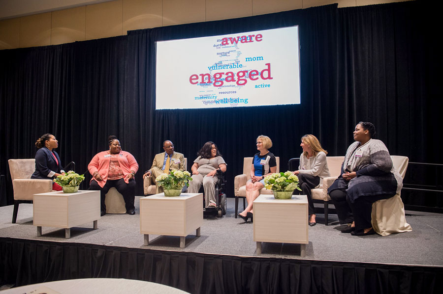 Panel moderator and six panelists, one of whom is in a wheelchair, on stage.