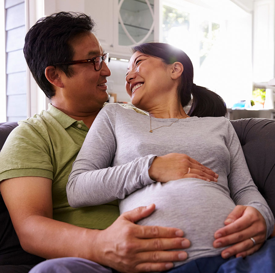 A pregnant woman seated with a man. Both are holding her belly.