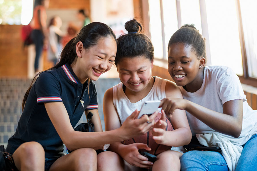 Three smiling young girls looking at smartphone.