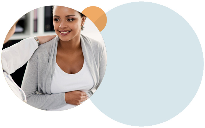 A healthcare provider with her arm on the shoulder of a pregnant woman who is holding her belly.