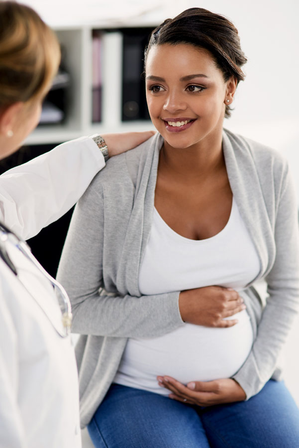 A healthcare provider with her arm on the shoulder of a pregnant woman who is holding her belly.