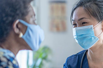 A woman speaking with a health care provider in an exam setting. Both people are wearing masks.
